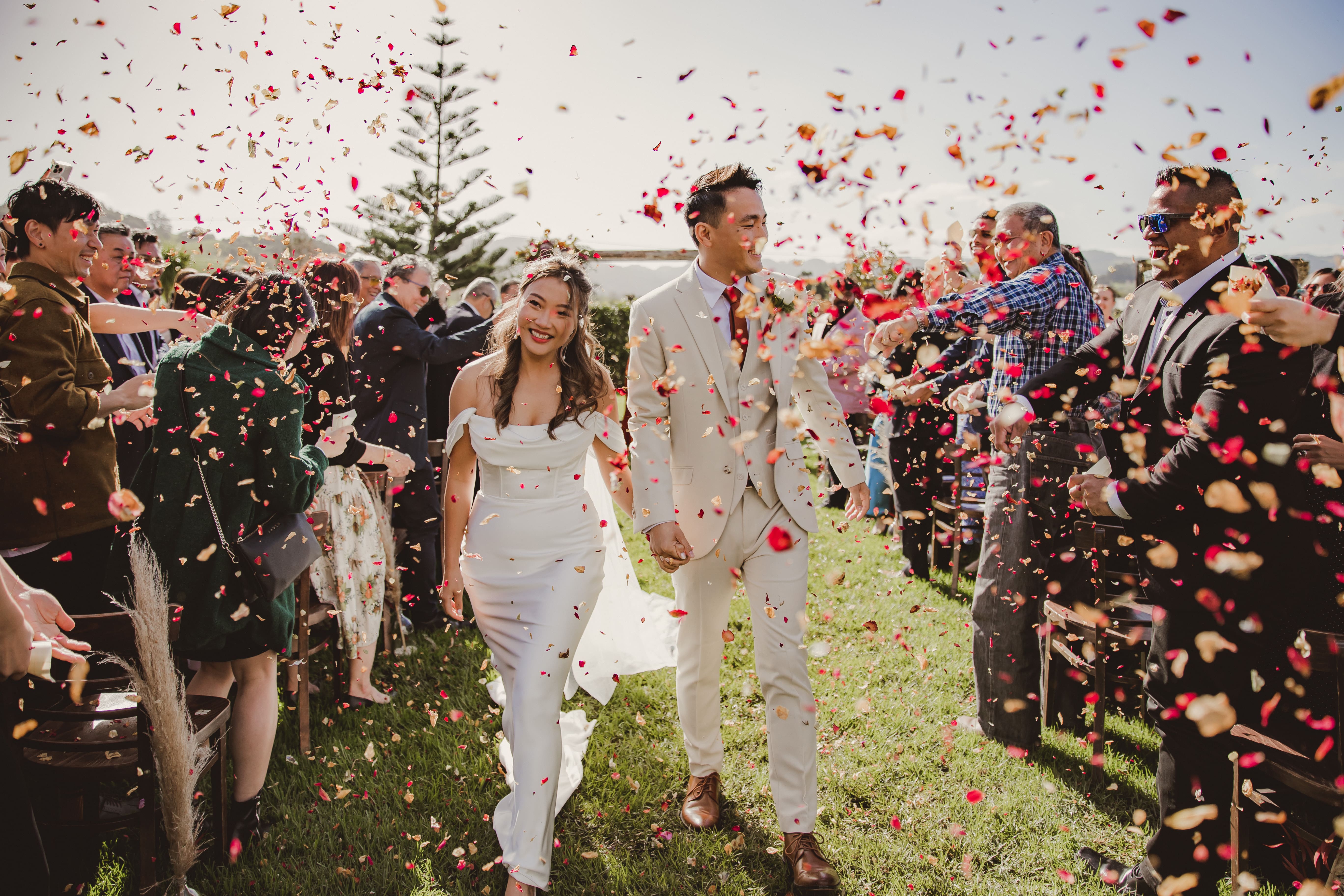 Bride and groom walking through a confetti toss with guests lining the path, outdoor wedding exit