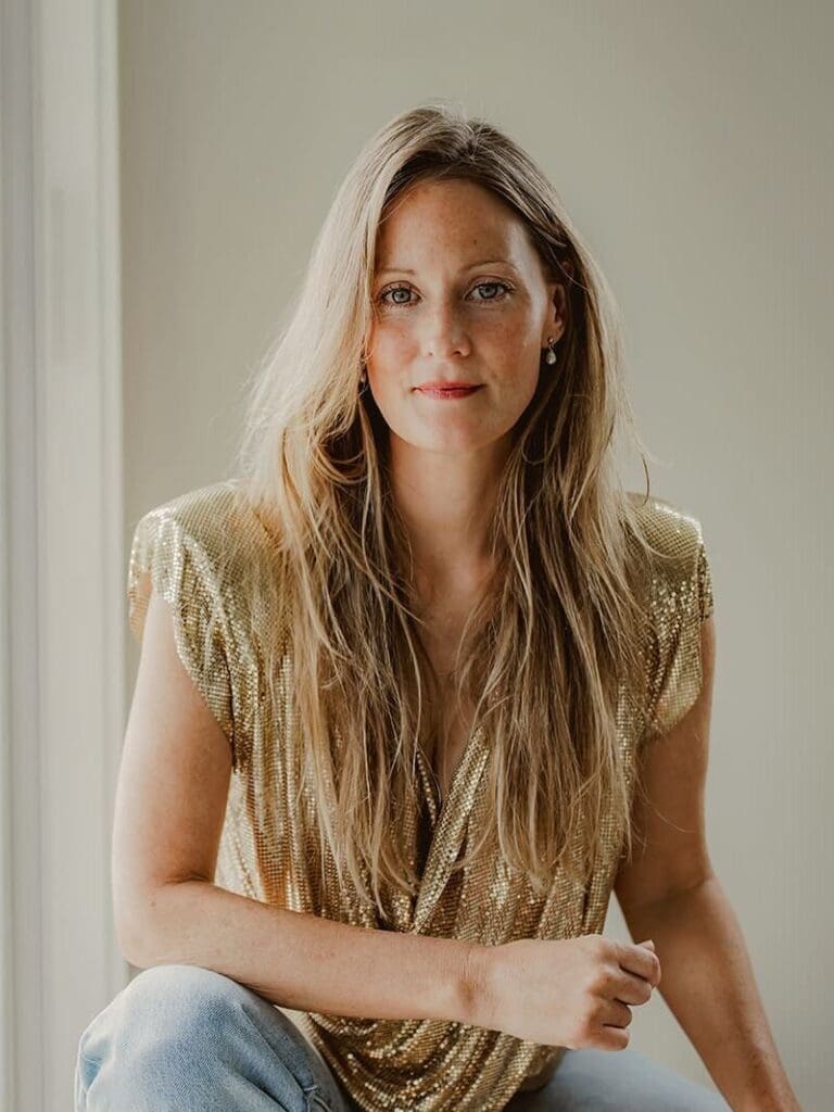 Personal branding portrait of a woman in a gold top, natural light against a soft neutral wall
