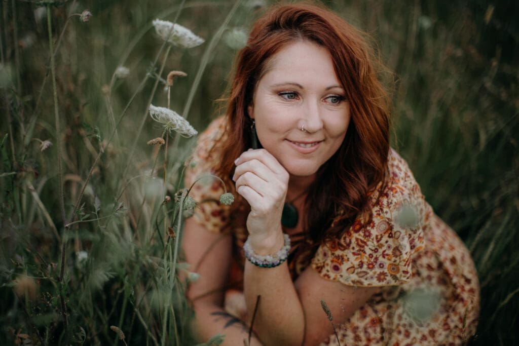 Kate Little Photography, personal branding portrait of Kate crouched in long grass and wildflowers, warm golden light
