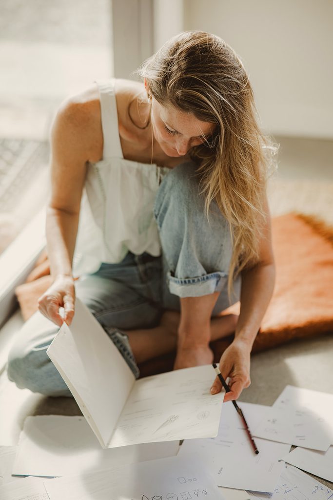 Personal branding lifestyle shot of a woman sketching in a journal, sitting on the floor in soft natural light