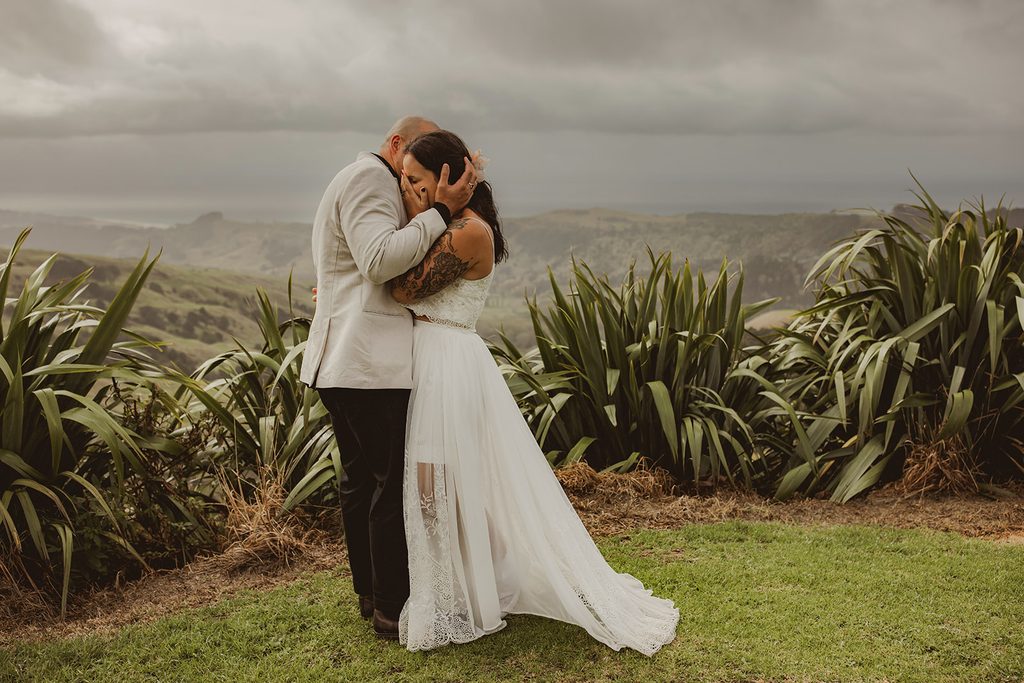 Bride and groom kissing on the hilltop at Vanderosa Farms, moody clouds rolling over the coastal view