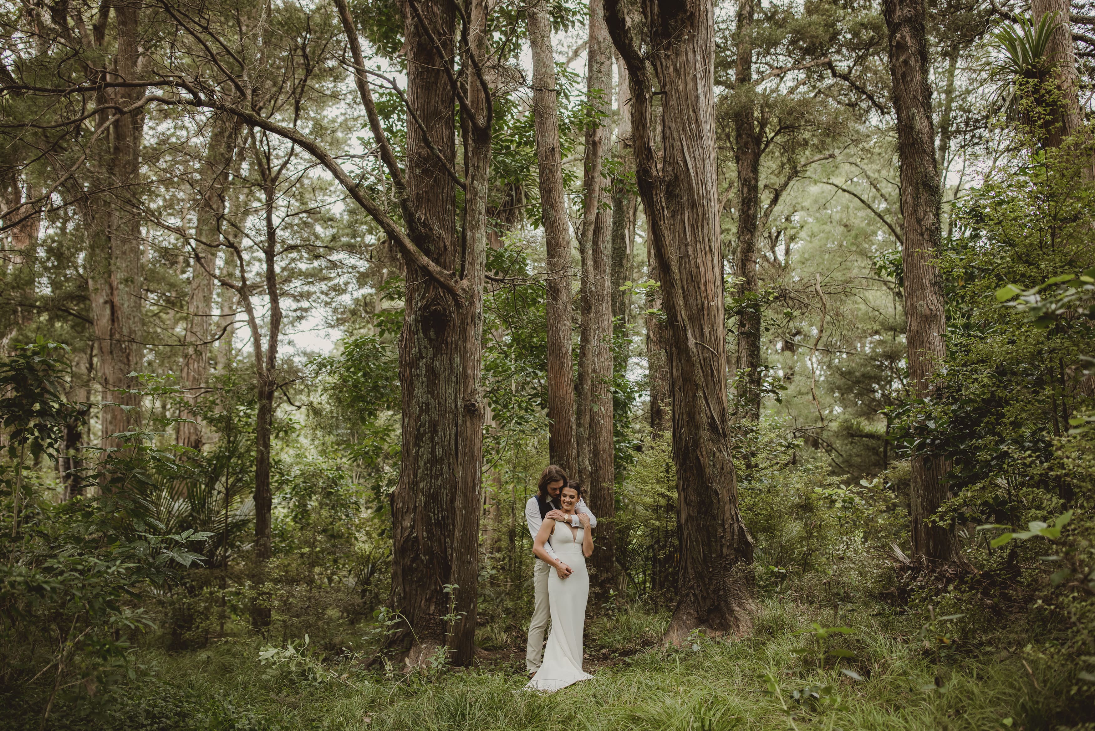 Bride and groom embracing in a native forest clearing near Plume, soft green woodland wedding portrait