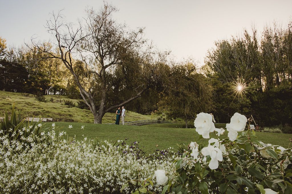 Couple sharing a quiet moment under a tree at Songbird Retreat, golden hour sun flare with white garden flowers in the foreground