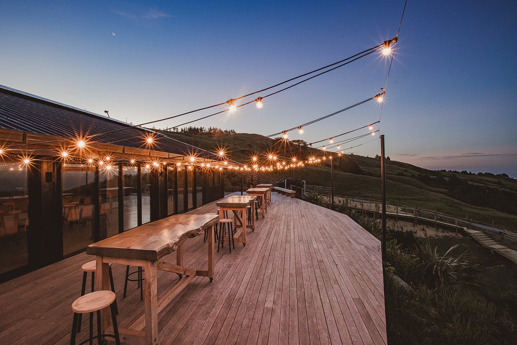reception deck at Vanderosa Farms strung with fairy lights at dusk, sweeping hill and coastal views under a crescent moon"