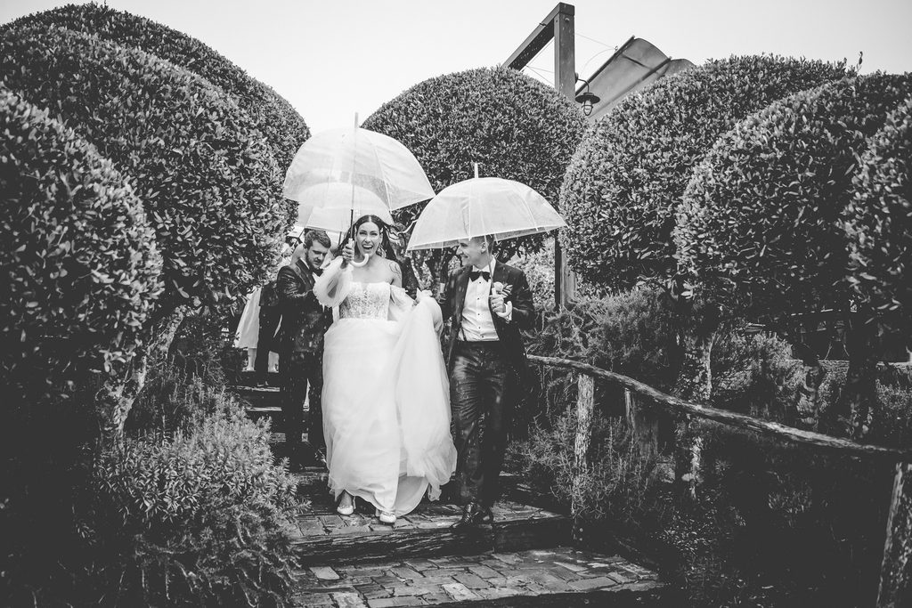 Bridal party walking down the steps at Mudbrick Vineyard under umbrellas on a rainy wedding day, Waiheke Island wedding photographer
