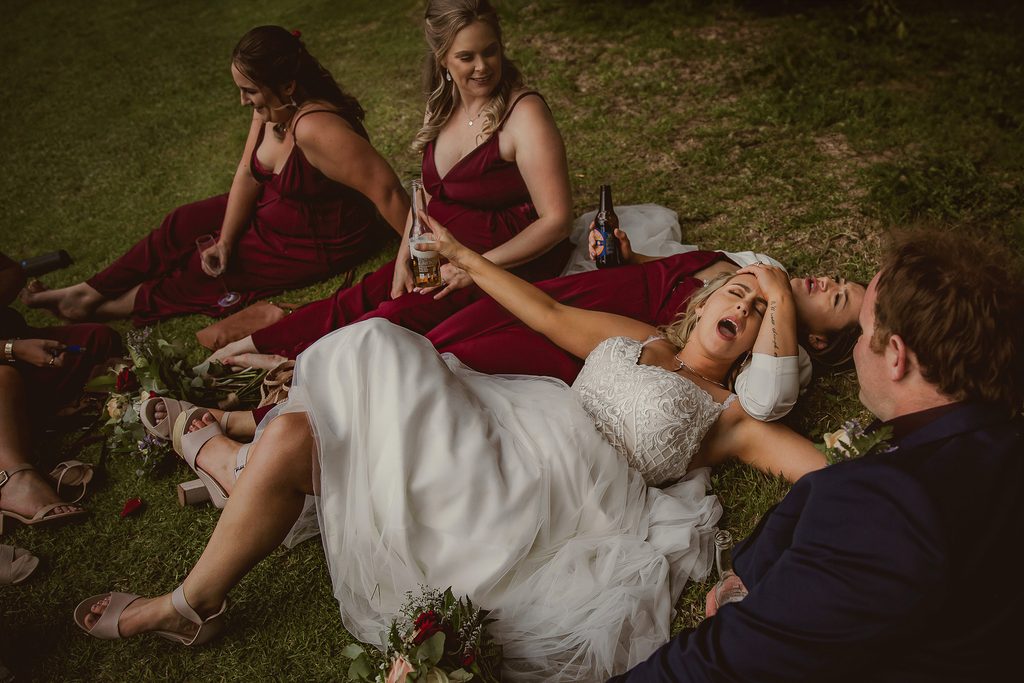 Bride laughing on the grass with bridesmaids in burgundy dresses, candid in-between moment at a New Zealand wedding"