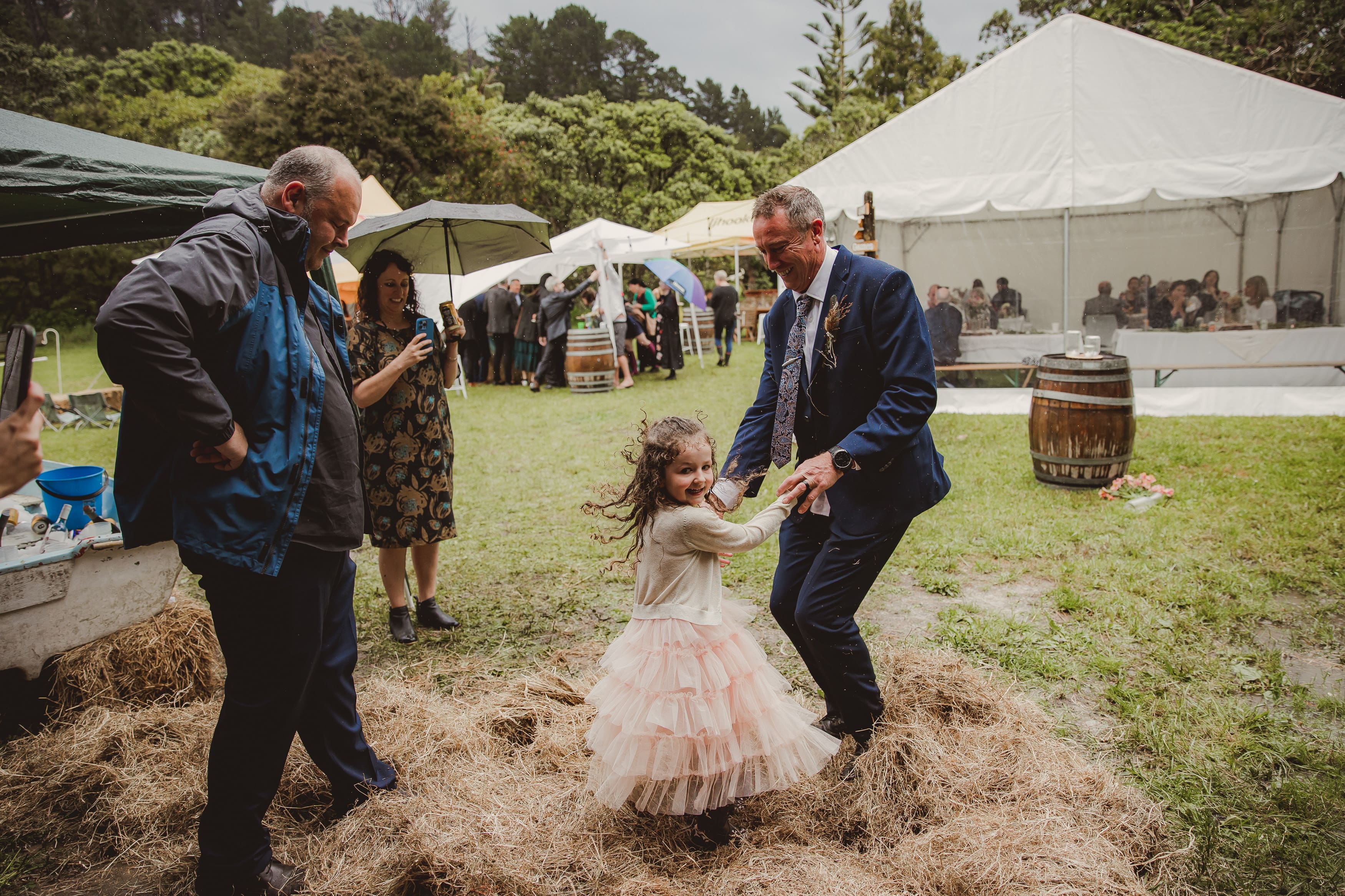 Groom and his daughter jumping in a puddle with hay at rainy wedding on Matakana Coast 